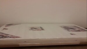 Ein Zimmer mit einem Bett, bezogen mit einem weißen Bettlaken und einem Matratzenschoner.