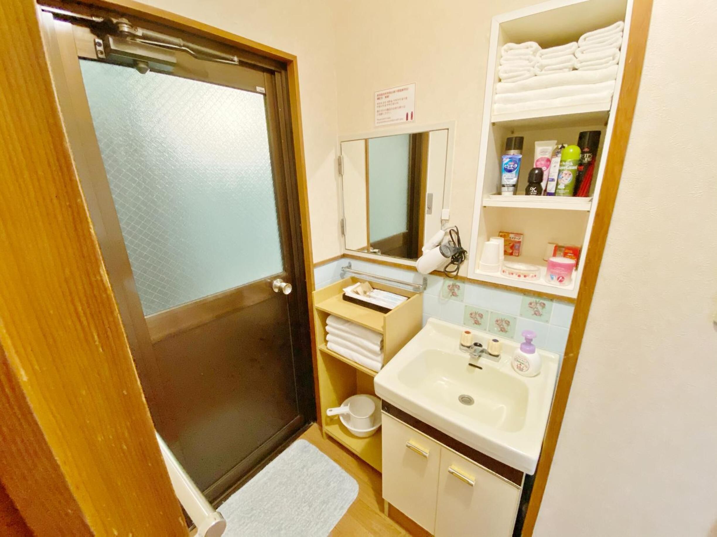 A compact bathroom with a shower, a sink, and a mirror. There are towels and toiletries on shelves.