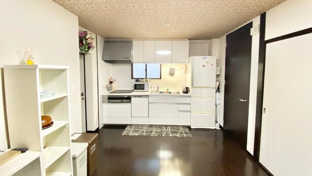 A modern kitchen with white cabinets, a microwave, and a refrigerator. There is a skylight above the kitchen, and the floor is dark wood. - Guesthouse 017 Reina (Tokushima)
