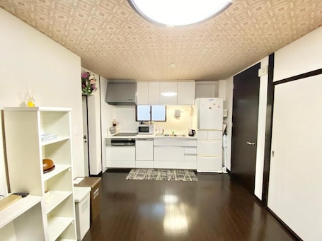 A modern kitchen with white cabinets, a microwave, and a refrigerator. There is a skylight above the kitchen, and the floor is dark wood.