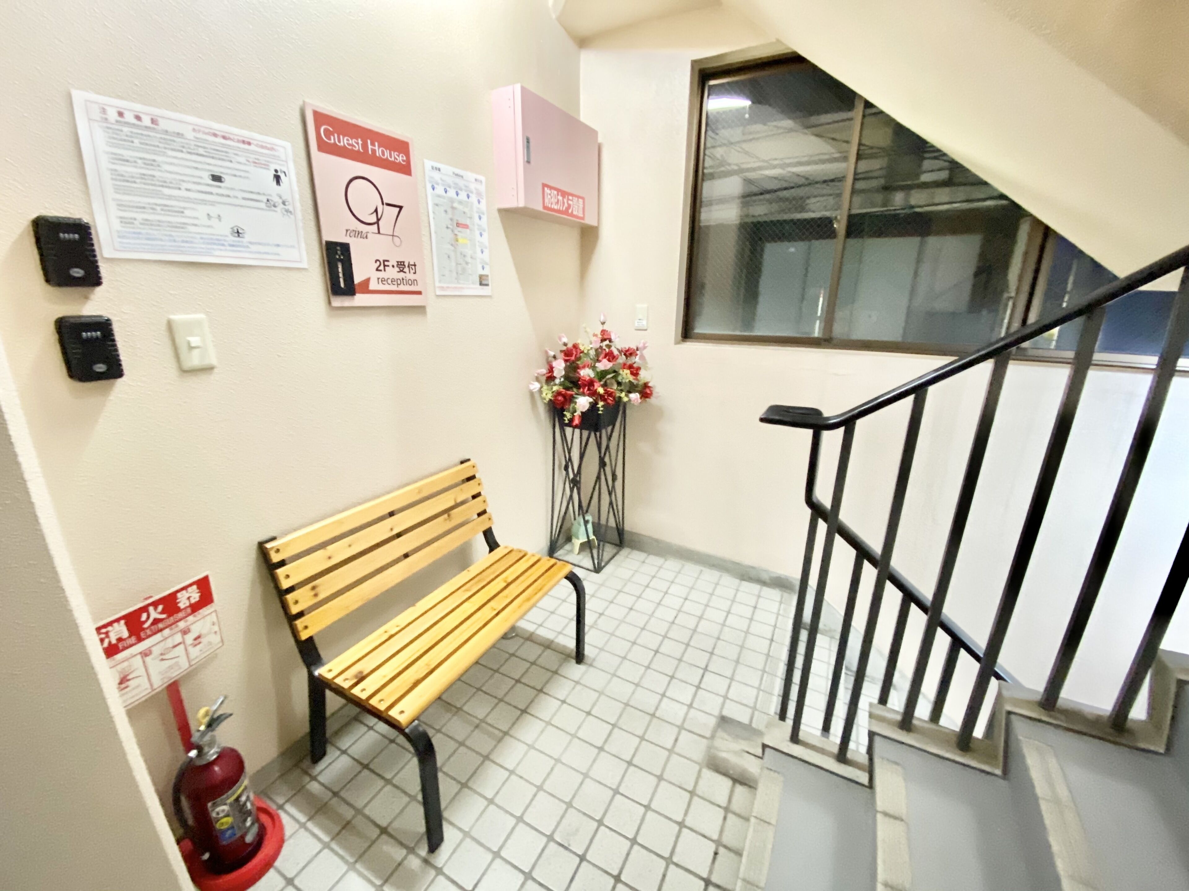 Un banc dans un couloir, avec un extincteur, un arrangement floral et des panneaux indiquant l’emplacement de la réception et des chambres d’hôtes.