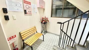 Un banc dans un couloir, avec un extincteur, un arrangement floral et des panneaux indiquant l’emplacement de la réception et des chambres d’hôtes.