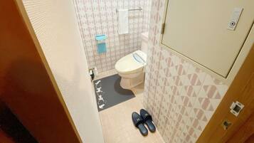 Un baño pequeño con un inodoro, un perchero para toallas y un par de pantuflas en el suelo.