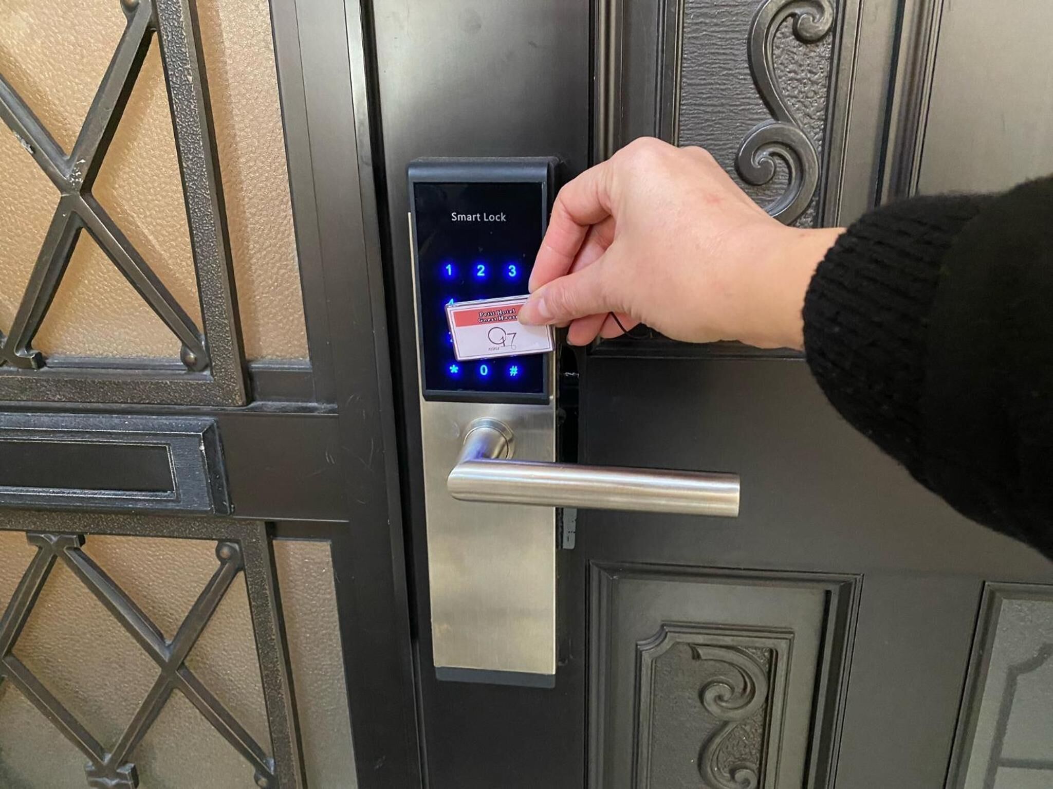 A hand using a smart lock on a door with a keypad and a metallic handle.
