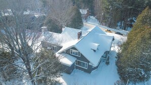 A snow-covered house with a steep roof, surrounded by trees and a clear sky. -  Walk to Village View Lake Placid Hot Tub, Fire Pit, Volleyball, kids playground (Lake Placid)