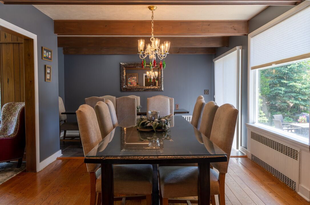 Une salle à manger avec une table en bois foncé, six chaises, un lustre et une grande fenêtre donnant sur un paysage verdoyant.