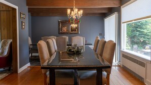 A dining room with a dark wooden table, six chairs, a chandelier, and a large window with a view of greenery. -  Walk to Village View Lake Placid Hot Tub, Fire Pit, Volleyball, kids playground (Lake Placid)