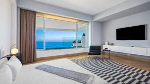 A modern hotel room with a large window, a flat-screen TV, a bed, and a seating area.