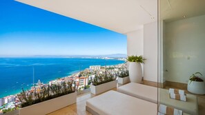 A balcony with a city view, white furniture, and potted plants.