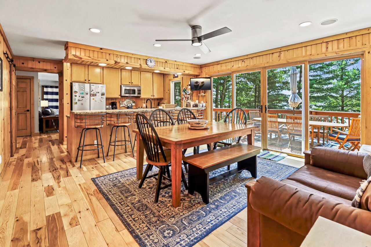 Une cuisine spacieuse avec des meubles en bois, un coin repas doté d’une grande table et de chaises, et un coin salon confortable avec un canapé en cuir marron.
