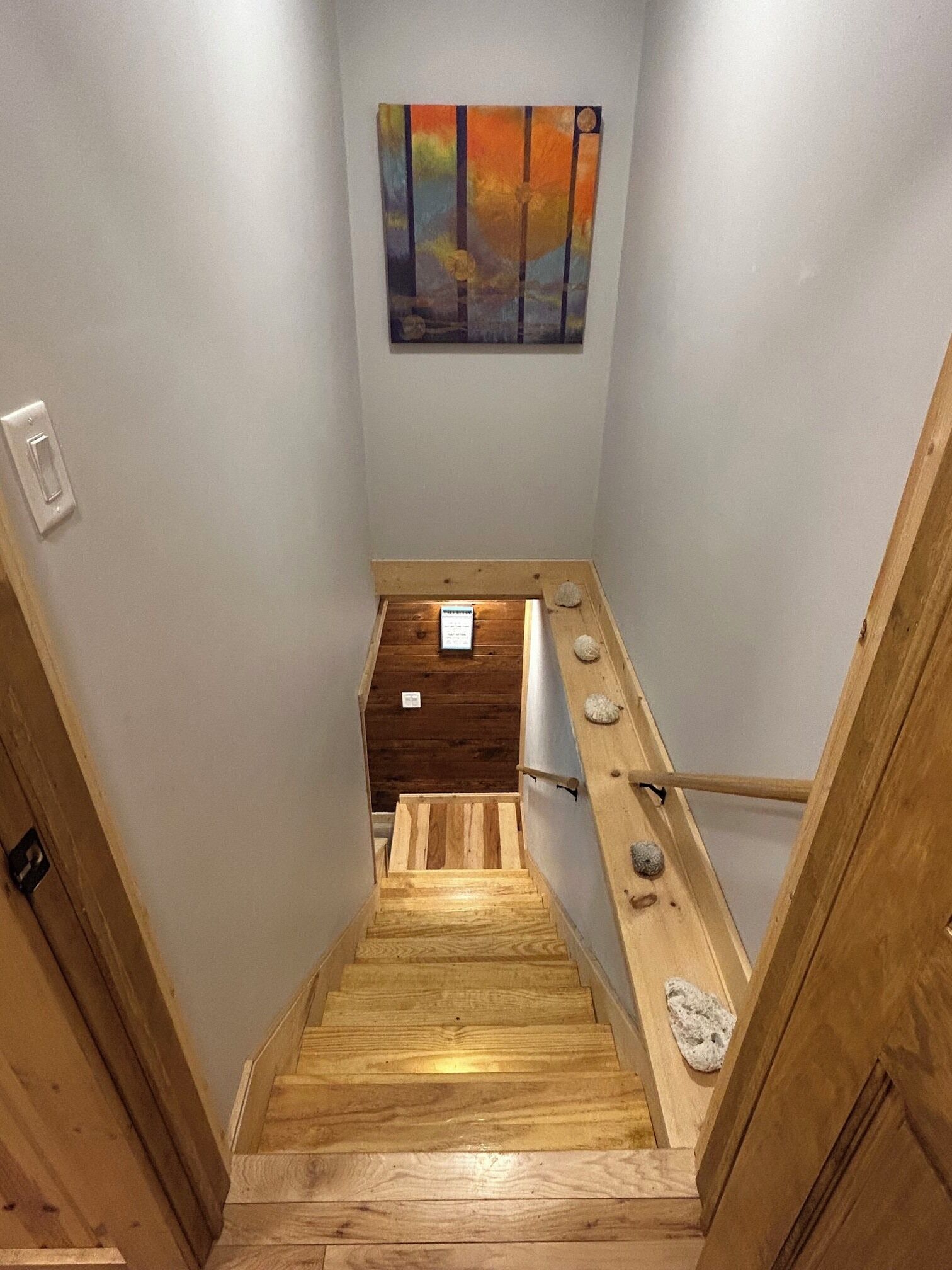 A wooden staircase with a handrail, a small wooden box on the landing, and a painting on the wall.