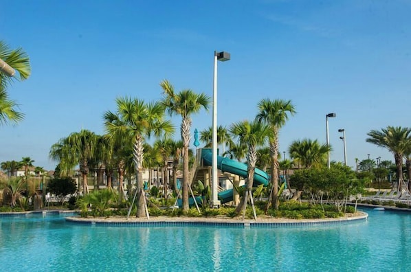 A swimming pool with a water slide, surrounded by palm trees and a clear sky.