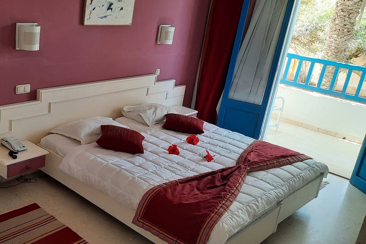 Ein Hotelzimmer mit einem großen Bett, Nachttischen, einem Telefon und einem Fenster mit Blick nach draußen.