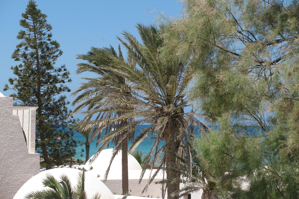 A resort with palm trees, a clear blue sky, and a view of the sea.