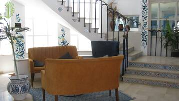 Amplia sala de estar con escalera, un sofá, una silla y un jarrón decorativo.