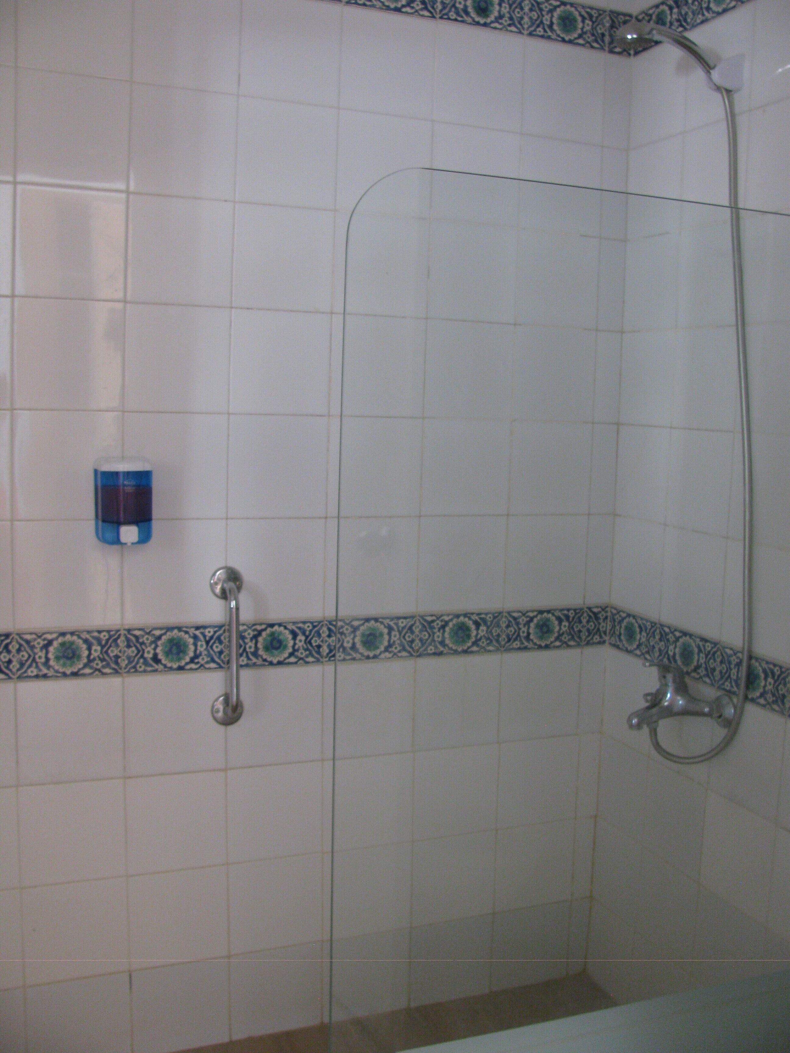 A bathroom with white tiled walls, a shower with a glass door, and a corner with a decorative blue and white tile border.