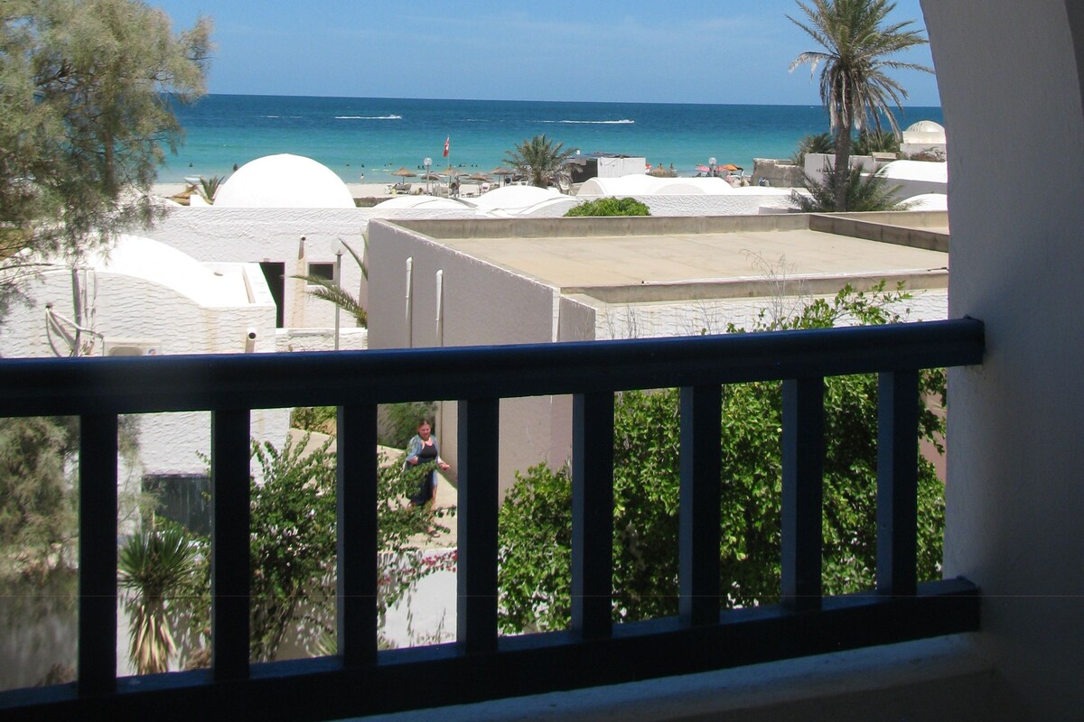 A balcony with a view of the sea and a white building with a dome structure.