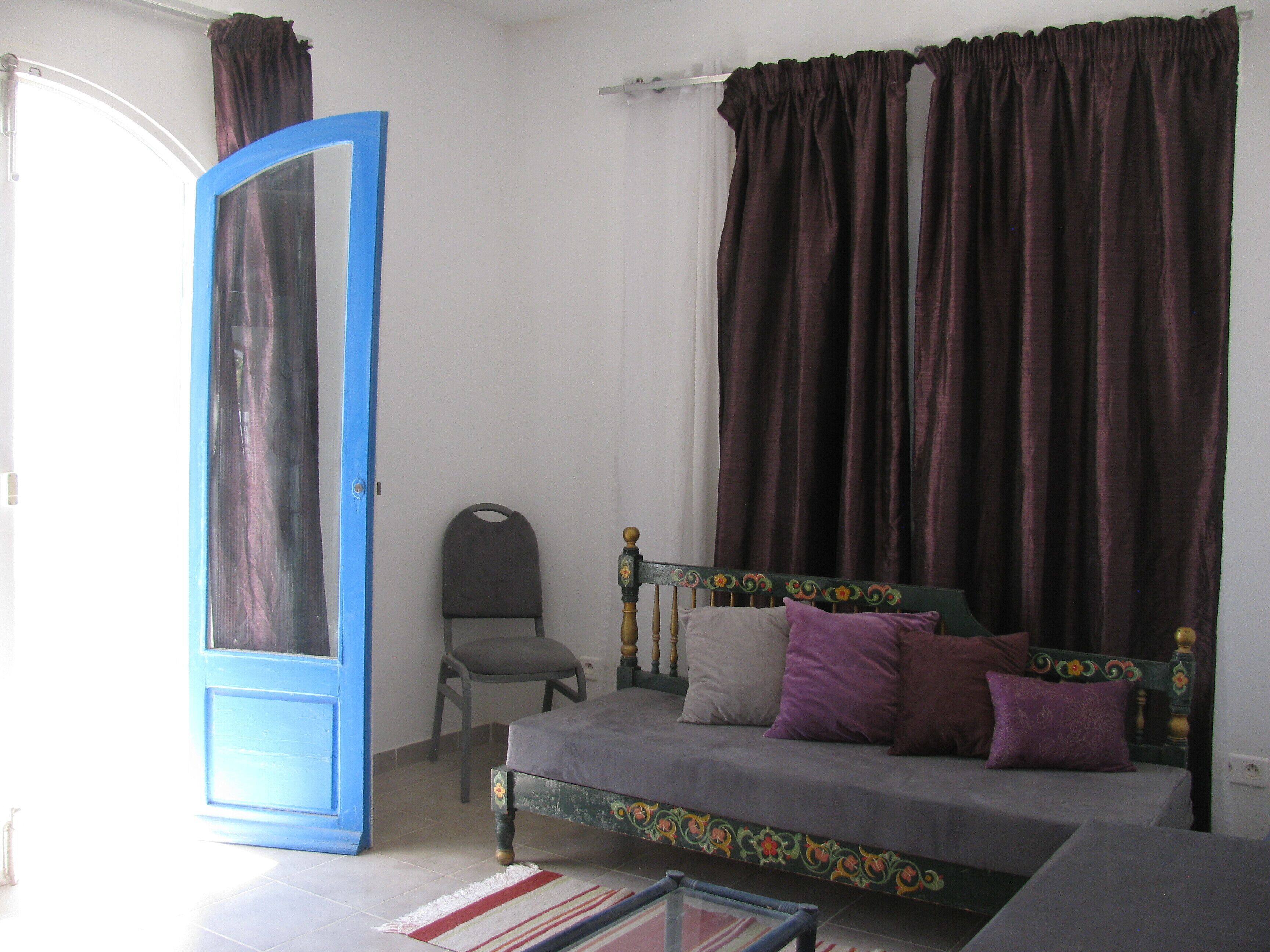 A bedroom with a bed, a chair, a window with curtains, and a door.