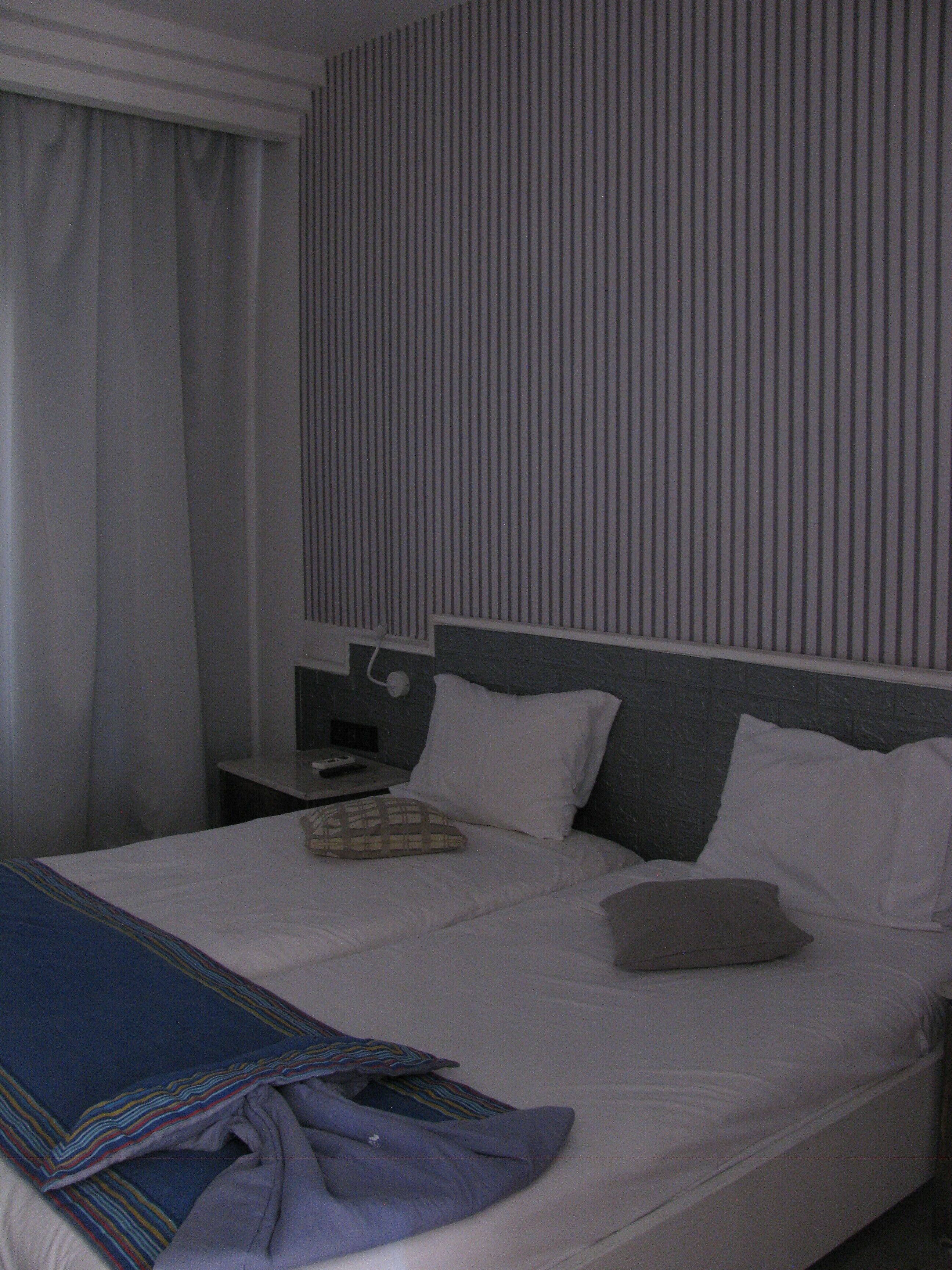 A hotel room with a bed, pillows, a nightstand, a lamp, and a curtain.