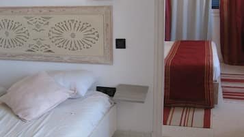 A bedroom with a bed, a nightstand, a wall-mounted lamp, and a red-striped rug.