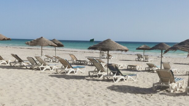 A beach with rows of sun loungers and thatched umbrellas. - Dar Salem (Mezraia)