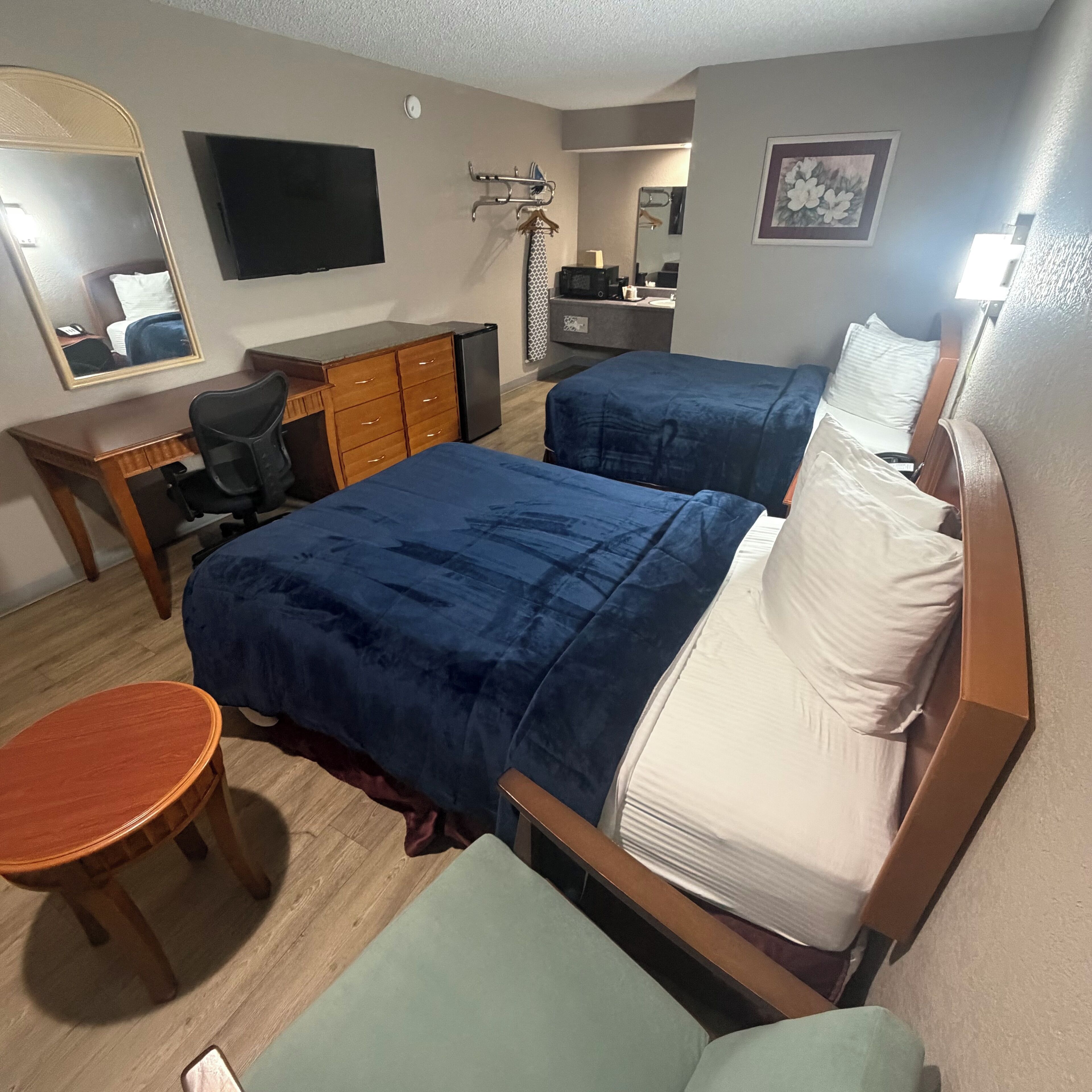 Ein Hotelzimmer mit zwei Betten, einem Schreibtisch, einem Stuhl, einer Kommode, einem Fernseher und einem Badezimmer.