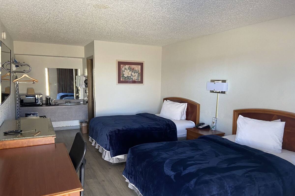 A hotel room with two beds, a desk, a mirror, a framed picture, and a bedside lamp.