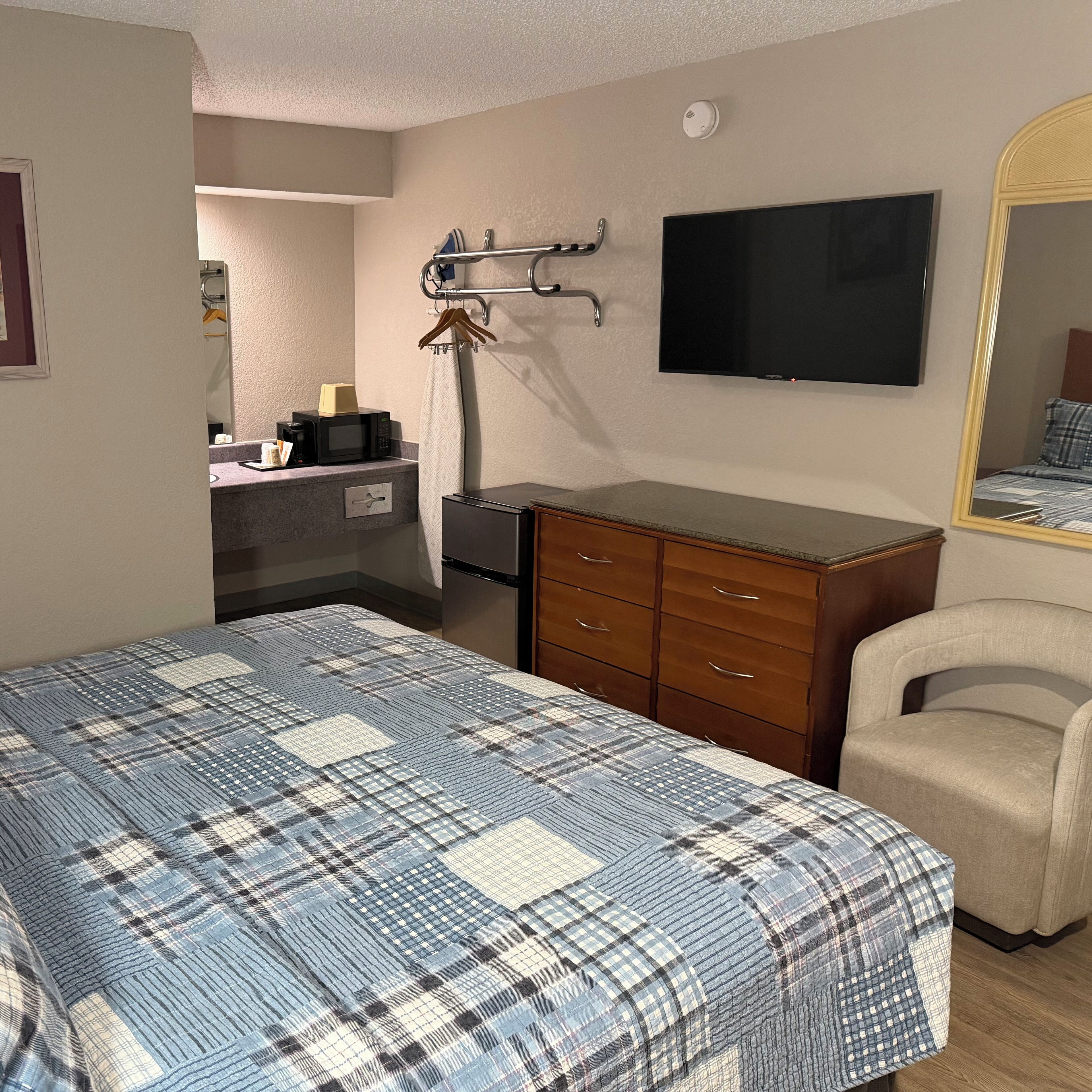 A bedroom with a bed, dresser, chair, and a TV mounted on the wall.