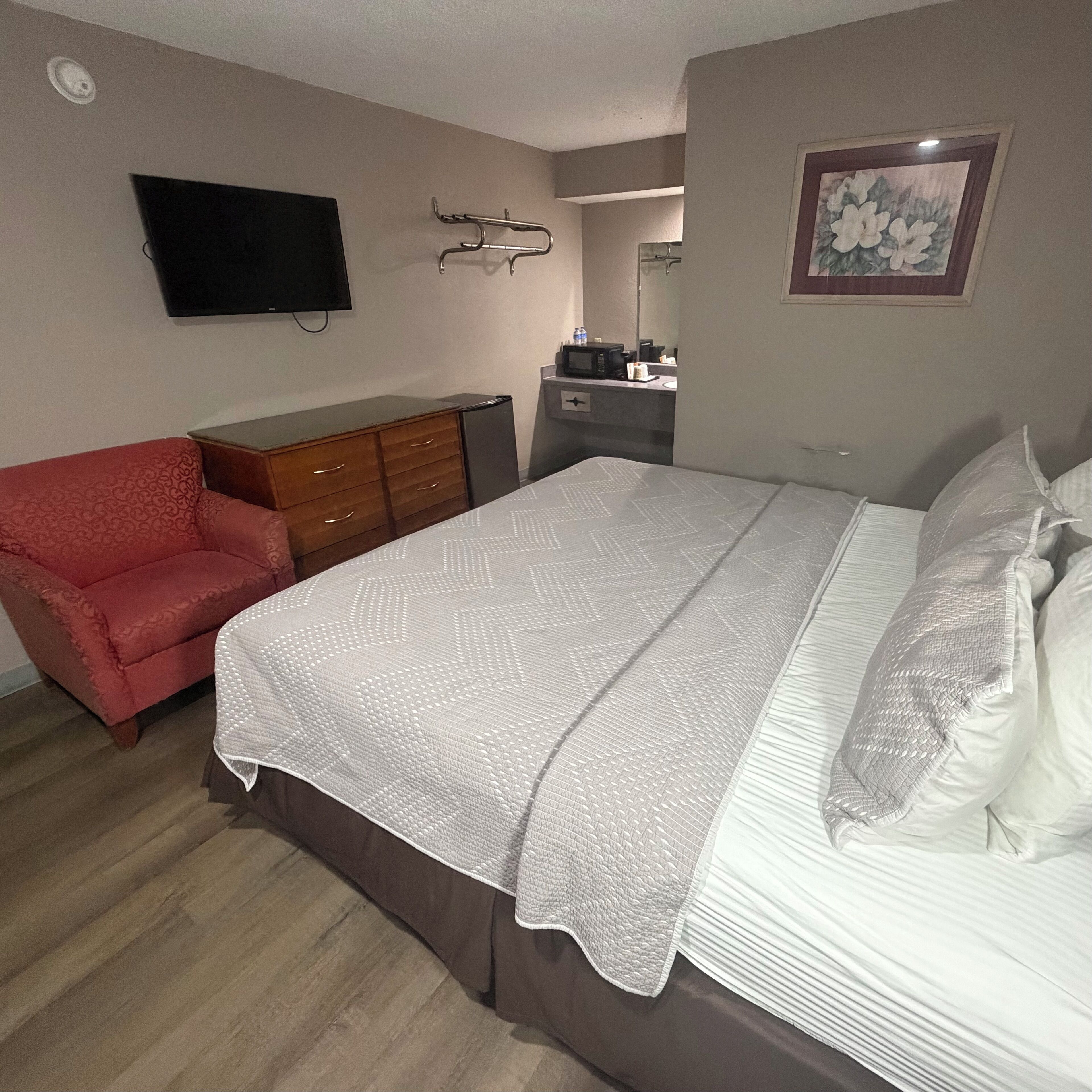 Una camera da letto con un letto, una cassettiera, una televisione, un forno a microonde e una poltrona rossa.