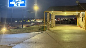 A Colonial Inn parking area at night with a blue illuminated sign, a covered parking structure, and a satellite dish on the roof.