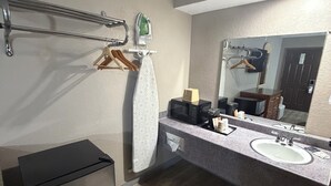 A modern bathroom with a built-in sink, a mirror, a towel rack, a microwave, and a small refrigerator.