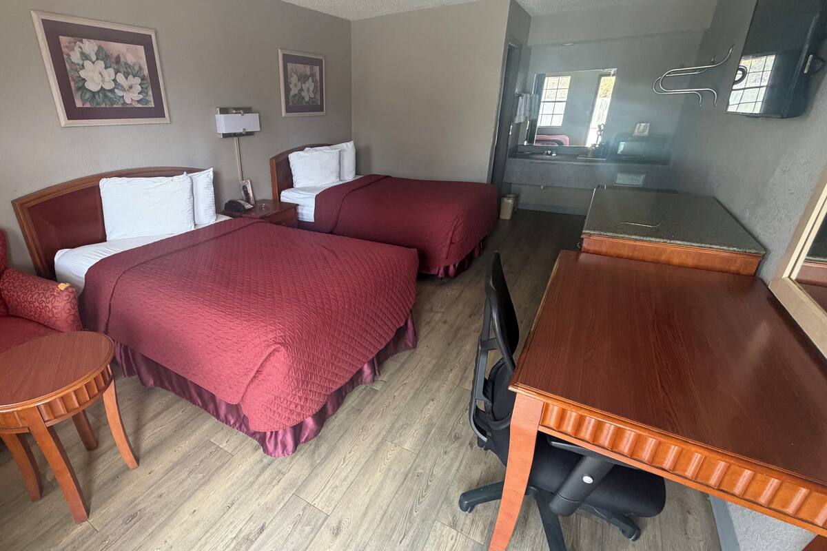 A hotel room with two beds, a desk, a chair, and a small table.