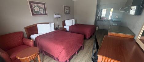 A hotel room with two beds, a desk, a chair, and a small table.