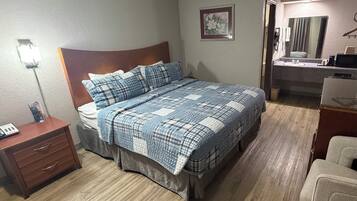 A bedroom with a bed, a nightstand, a dresser, a chair, a bathroom with a sink and mirror, and a painting on the wall.