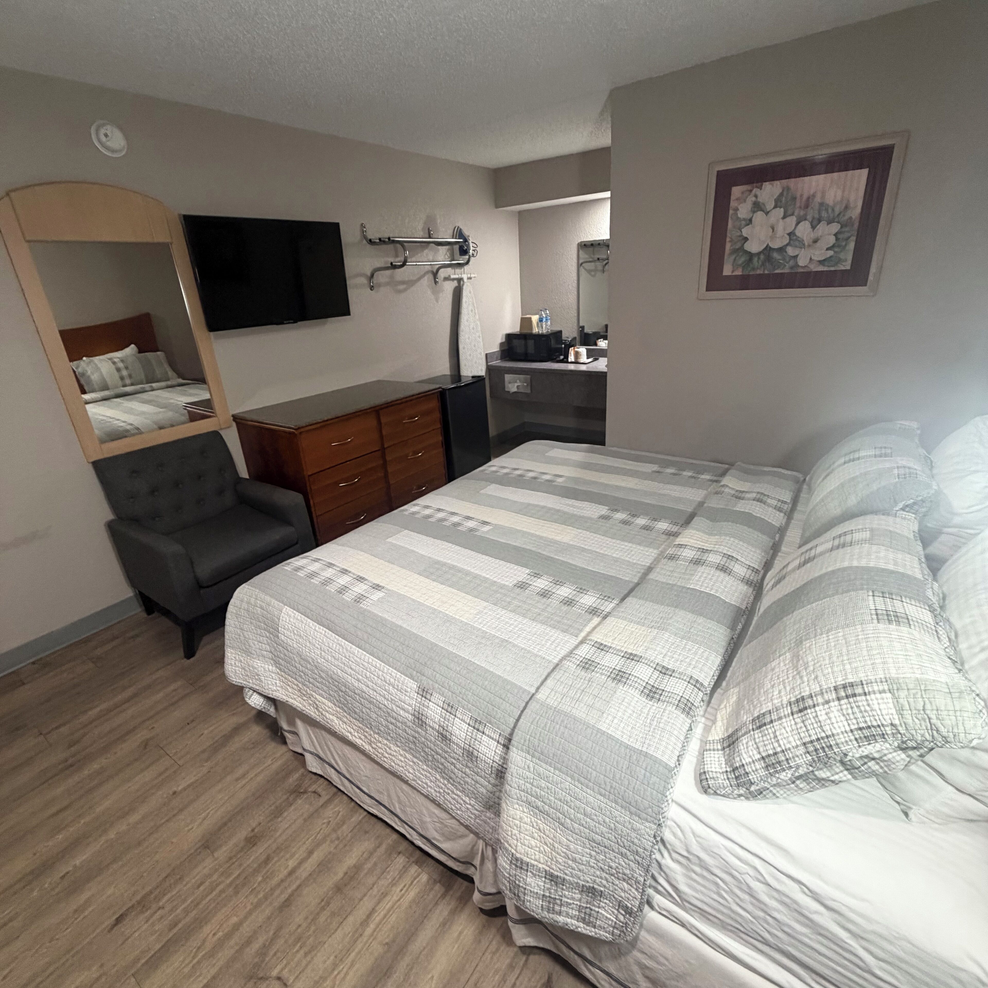 A bedroom with a bed, a dresser, a chair, a TV, and a mirror.