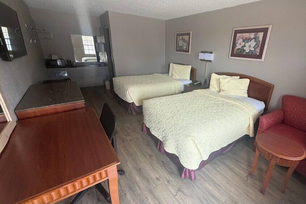 A hotel room with two beds, a desk, a chair, a mirror, and two wall-mounted paintings.