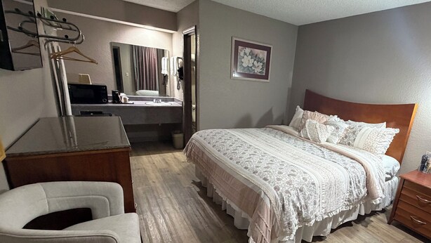 A bedroom with a bed, a desk, a chair, a dresser, and a bathroom with a sink and mirror.