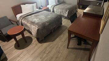 Habitación de hotel con dos camas, una mesita redonda pequeña, un escritorio de madera, un espejo y un baño con lavamanos y espejo.