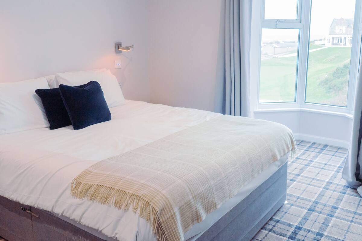 A bedroom with a bed, a window with curtains, and a view of a building outside.