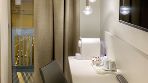 A hotel room with a white desk, a black chair, a TV mounted on the wall, and a window with curtains. - Agorà B&B Urban Relais (Canosa di Puglia)