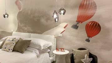 A modern bedroom with a bed, bedside tables, a small side table with a 'NOEL' decoration, and a wall mural of hot air balloons.