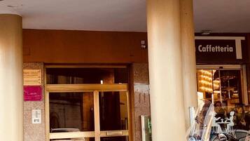 Entrada de um prédio com porta de vidro, placa indicando 'Caffetteria' e uma scooter estacionada.