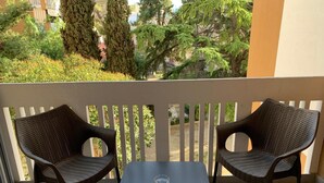 A balcony with two wicker chairs and a small table, overlooking a garden with trees and a building in the background. - Agorà B&B Urban Relais (Canosa di Puglia)