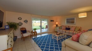 A living room with a sofa, a coffee table, a chair, a lamp, and a large window. - Cozy cottage in Gulf Gate to relax year-round in beautiful Sarasota. (Sarasota)
