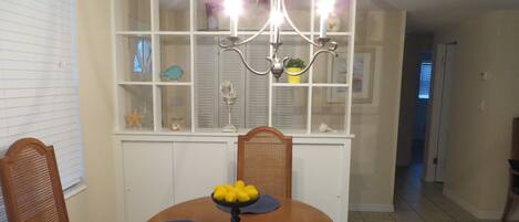 Un comedor con una mesa de madera, sillas, una araña y una estantería decorativa con varios objetos.