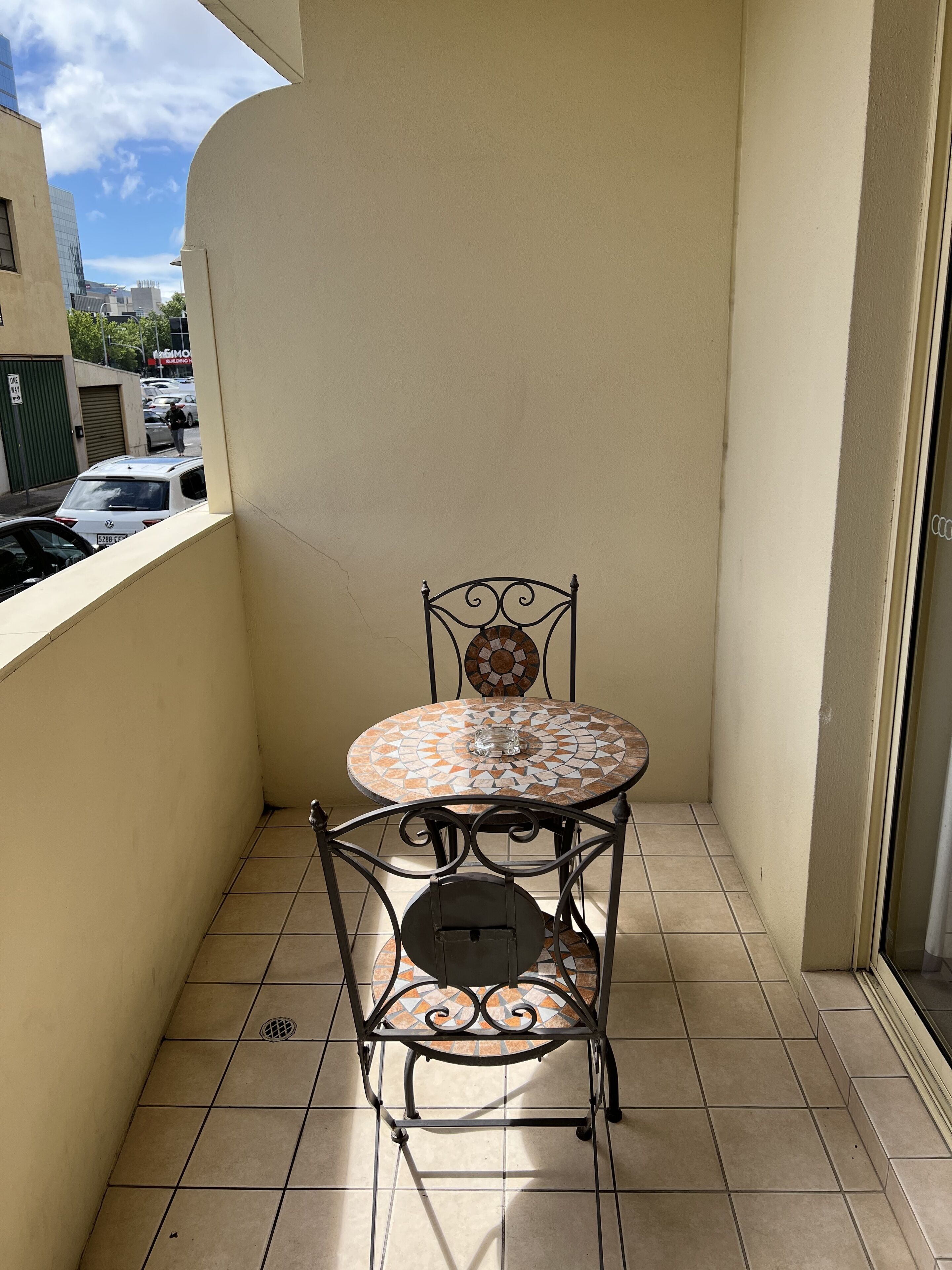A small balcony with a tiled floor, a metal chair, and a table with a mosaic top.