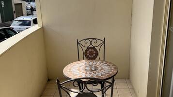 A small balcony with a tiled floor, a metal chair, and a table with a mosaic top.