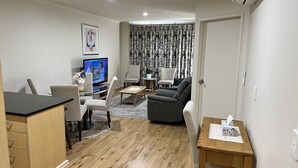 A modern living room with a flat-screen TV, grey sofas, a wooden coffee table, and a small dining table. - ADELAIDE CENTRAL APARTMENT - 3BR, 2BATH & CARPARK (Adelaide)