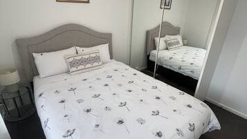 A neatly made bed with a floral bedspread, a bedside lamp, and a framed picture on the wall.