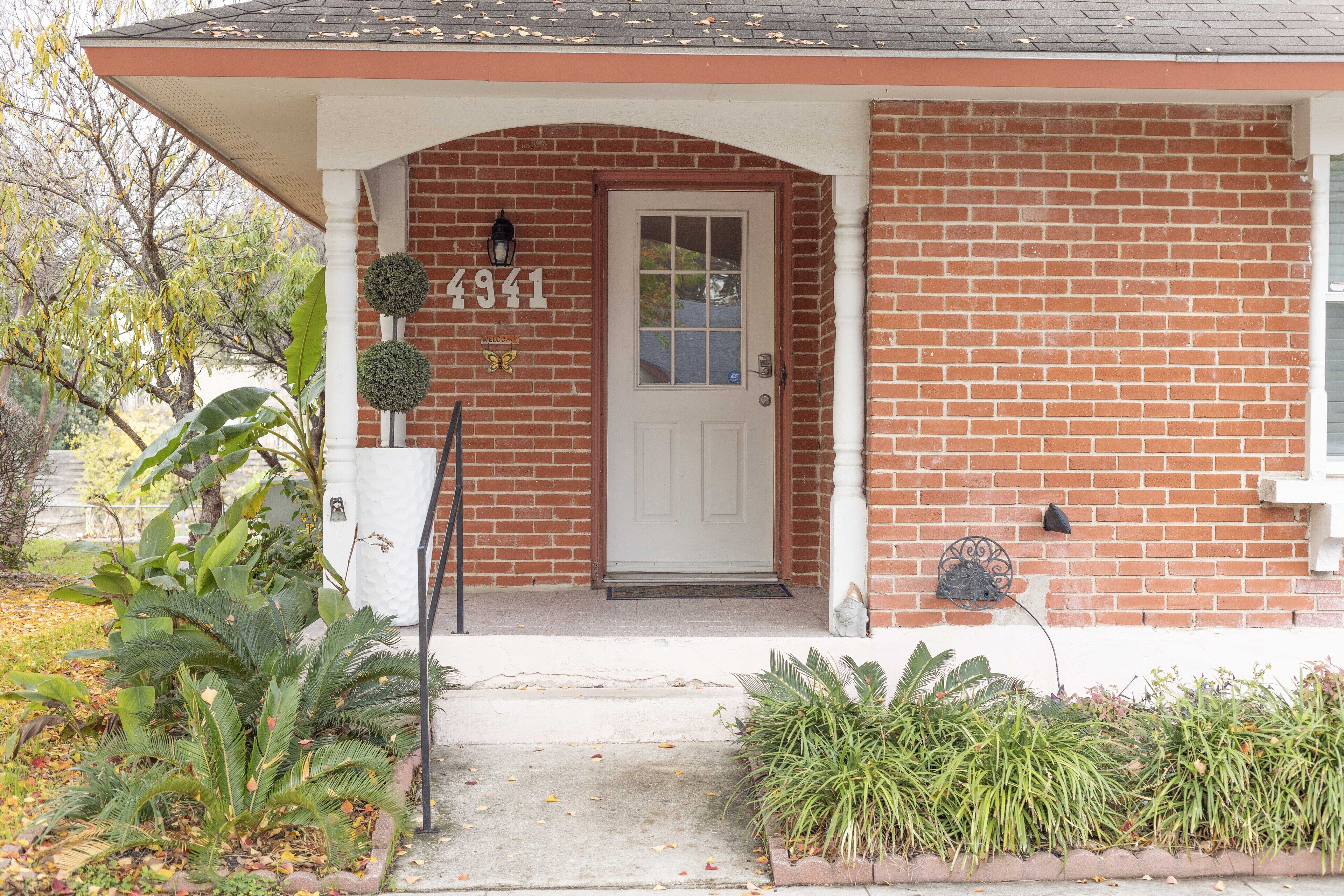 Une maison en briques avec une porte blanche, le numéro 4941, et un porche orné de plantes.